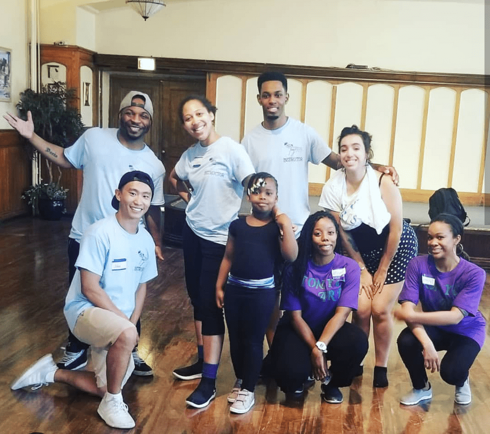 A group of dance teachers poses with a young black female student.