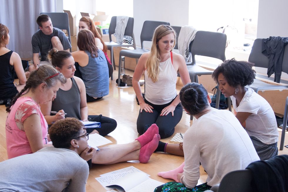 Women of various ages and ethnicities sit on the floor in a circle with notes.