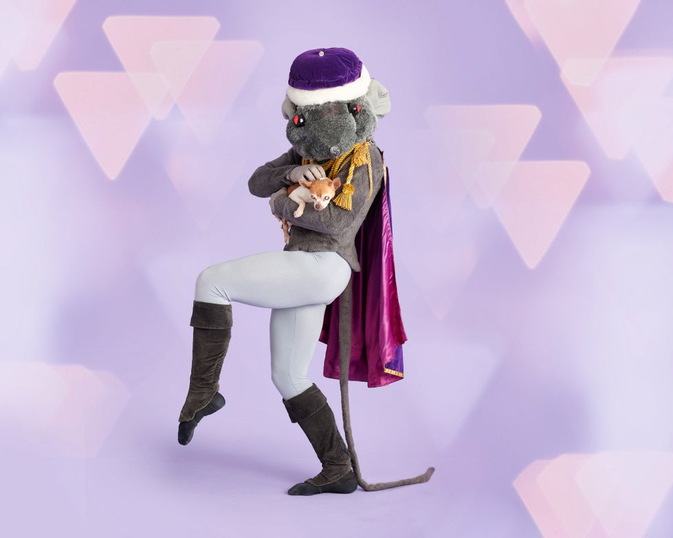 A dancer dressed in a rat costume holds a small, blind dog.