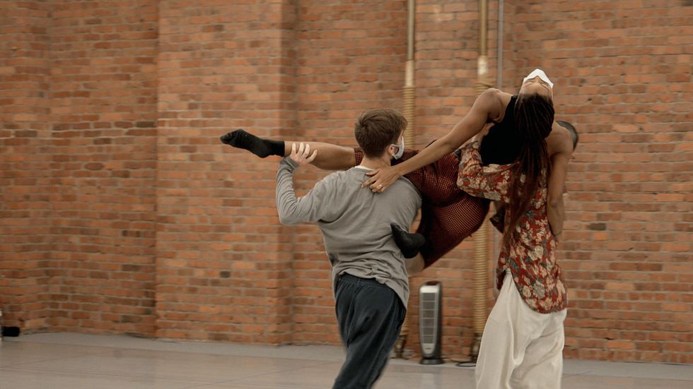 Two dancers lift a third above their shoulders as she arches her head back, one leg extended to the side