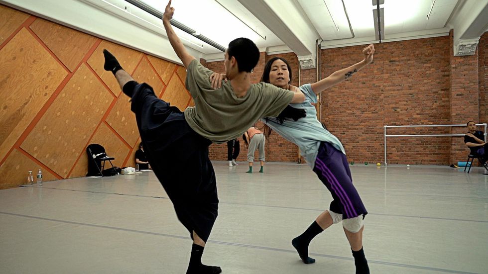 Two dancers grab each other's shoulders, reaching away from one another with their hips, free arms outstretched